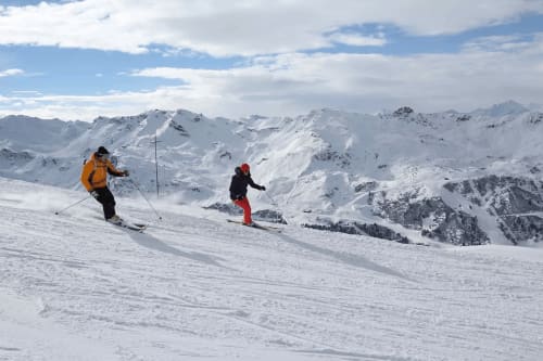 Deux skieurs descendant les pentes enneigées près de Méribel avec les pics alpins et le ciel bleu