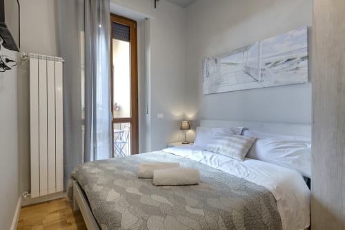 Luminosa camera da letto in BnB a Firenze con balcone, biancheria bianca, testata moderna, arredamento con vista giardino e pavimenti in legno.