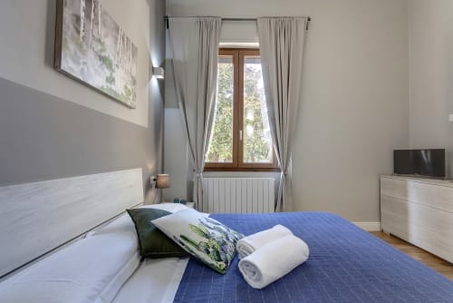 Bright bedroom at Sleep tight Florence B&B in Firenze with blue bedspread, white pillows, wooden doors, and TV.