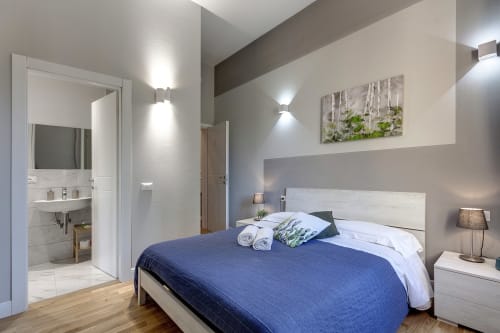 Modern bedroom at Sleep tight Florence with blue bedding, white headboard, ensuite bathroom, and contemporary lighting in