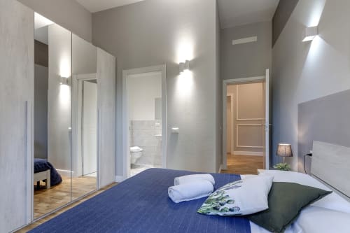 Modern bedroom at Sleep tight Florence with blue bed, white pillows, ensuite bathroom, and mirrored wardrobe in Firenze