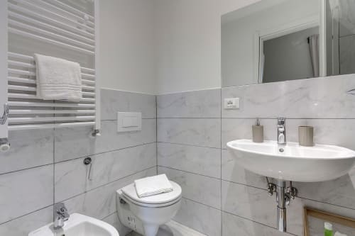 Modern bathroom at Sleep tight Florence with marble tiles, white sink, toilet, and shower with glass enclosure in Firenze
