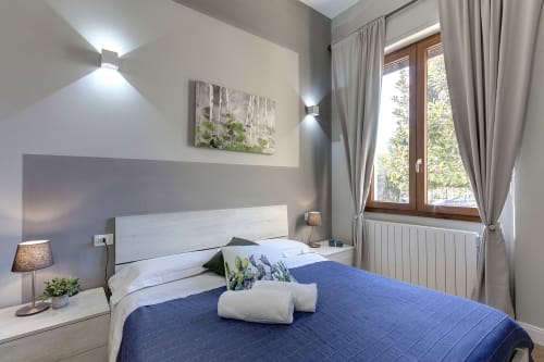 Modern bedroom at Sleep tight Florence with blue bedding, white headboard, wooden windows, and contemporary wall lighting