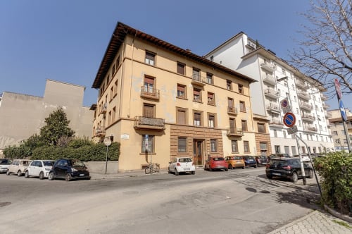 Yellow Renaissance building housing Sleep tight Florence BnB in Firenze with parked cars and modern apartments nearby