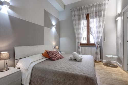 Camera da letto luminosa e moderna presso Sleep Tight Florence con letto bianco, cuscini decorativi rigati, pavimento in legno e luce naturale da