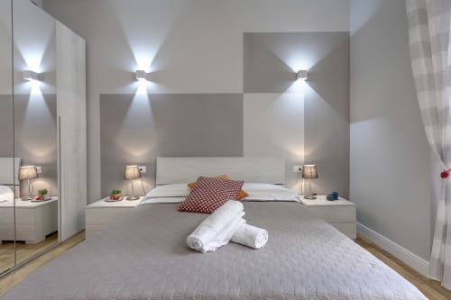 Camera moderna a Sleep tight Florence con letto bianco, applique murale, asciugamani arrotolati e parete con motivi geometrici a Firenze