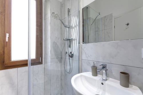 Bagno moderno nel Sleep Tight Florence B&B a Firenze con doccia in marmo, lavabo bianco, rubinetteria cromata e luce naturale dalla finestra.