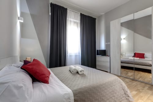 Camera moderna di Sleep tight Florence con letto, guardaroba a specchio, tende nere e pavimento in legno chiaro a Firenze.