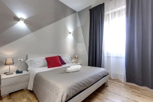 Camera moderna al Sleep tight Florence B&B a Firenze con biancheria bianca, cuscino rosso decorativo, soffitto spiovente e luce naturale