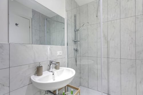 Bagno moderno con piastrelle di marmo, lavabo ovale bianco e box doccia in vetro presso Sleep tight Florence BnB a Firenze