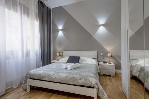 Camera moderna al Sleep tight Florence con letto bianco, pareti inclinate, applique murali, pavimento in legno e grandi finestre