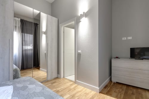 Camera da letto moderna a Sleep Tight Florence con armadio a specchio, pavimenti in legno, TV e cassettone a Firenze, Italia
