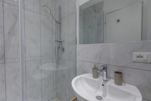 Moderno bagno presso Sleep tight Florence con piastrelle in marmo, doccia a filo, lavabo bianco e finiture cromate