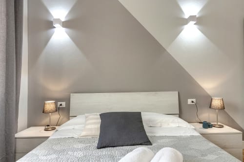 Camera da letto moderna in mansarda presso Sleep tight Florence con soffitto spiovente, due lampade, cuscino scuro decorativo e parete contemporanea