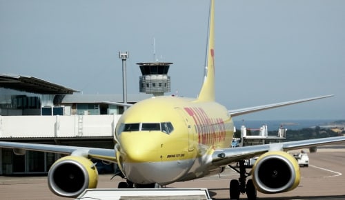 Avion Boeing 737 jaune à la porte d'embarquement de l'aéroport avec la tour de contrôle en arrière-plan