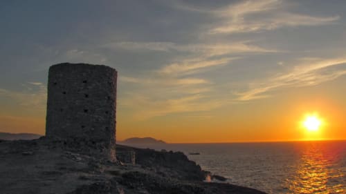 Tour en pierre ancienne silhouettée au coucher de soleil surplombant la Méditerranée près de Corbara, Corse