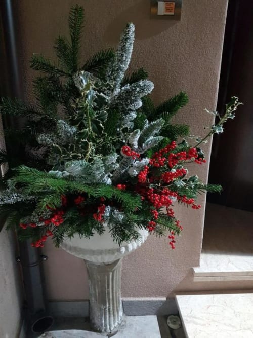 Composizione floreale natalizia con bacche rosse, rami sempreverdi e dettagli argentati in un'urna di pietra a B&B Emozioni Relax