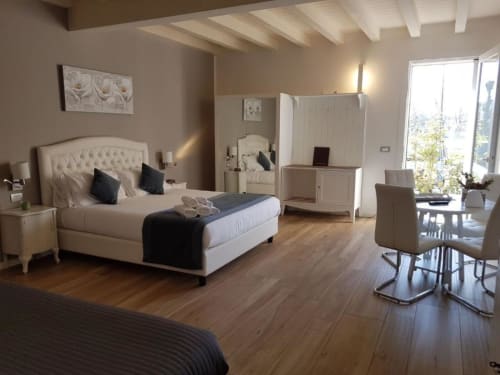 Camera elegante al B&B Emozioni Relax di Mantova con letto imbottito color crema, arredi bianchi e pavimenti in legno