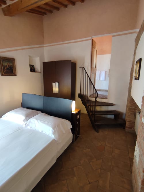 Camera da letto della Locanda del Vino Nobile a Montepulciano con letto, testata scura, scale in legno e pavimento in cotto