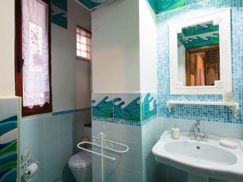 Bright turquoise bathroom in Orso Luxury Apartments Roma with tiled walls, white sink, mirror, and decorative toilet brush