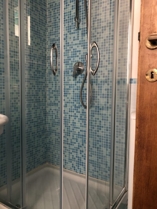 Modern glass shower enclosure with blue mosaic tiles in Roma luxury apartment bathroom