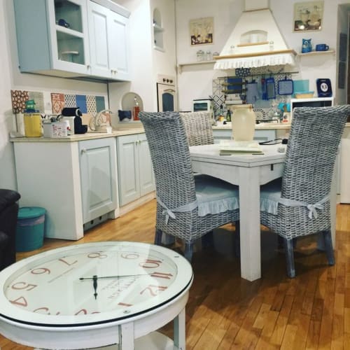Modern kitchenette with white cabinets, dining table, wicker chairs, and clock in Orso Luxury Apartments, Roma