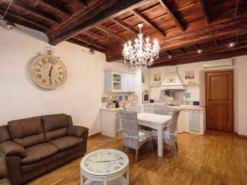 Rustic Rome apartment with exposed wood beams, chandelier, brown sofa, and modern kitchen at Orso Luxury Apartments