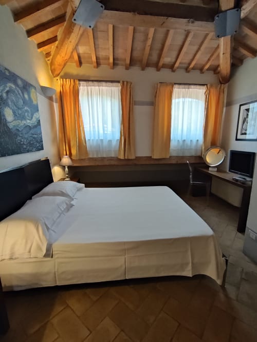 Elegante camera presso La Locanda del Vino Nobile a Montepulciano con travi in legno a vista, biancheria bianca e vista sulla città