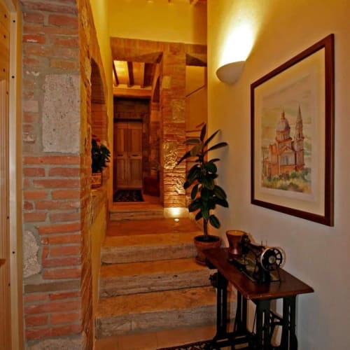 Accogliente corridoio della Locanda del Vino Nobile a Montepulciano con mattoni a vista, opere d'arte incorniciate e arredamento rustico
