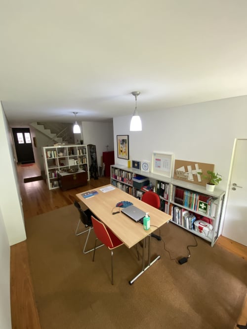 Bright common area at Casa45 Porto with wooden table, red chairs, bookshelves, and pendant lights