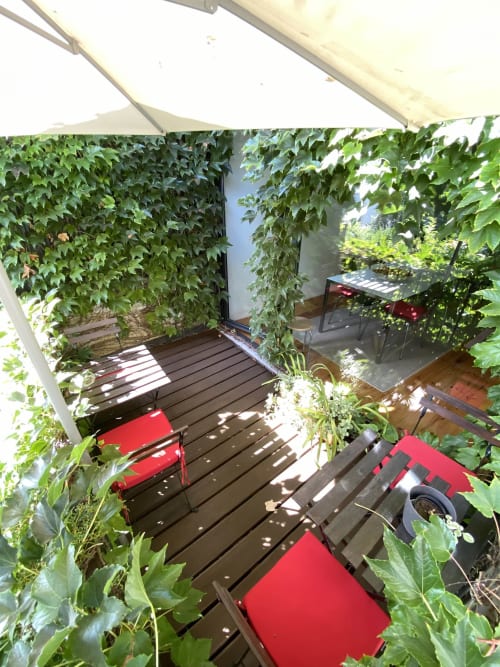 Shaded patio at Casa45 Porto with red chairs, dark decking, and climbing ivy creating a private garden retreat
