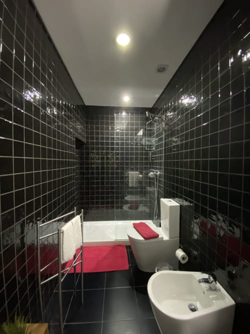 Salle de bains moderne aux carrelages noirs de la Casa45 Porto avec fixtures blanches, accents rouges et douche
