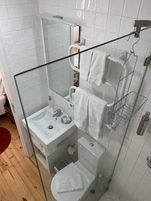 Salle de bain moderne et épurée à Casa45 Porto avec carrelage blanc, toilettes, petit lavabo, douche à l'italienne et serviettes blanches