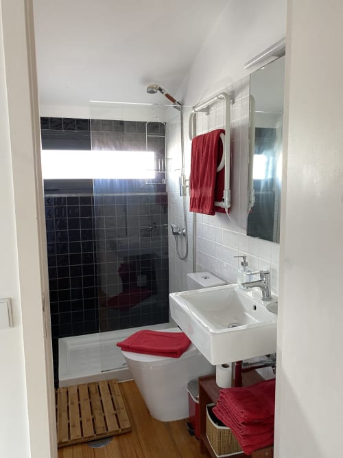 Salle de bain moderne à la Casa45 Porto B&B avec douche en carrelage noir, lavabo blanc, toilettes avec abattant rouge et sol en bois