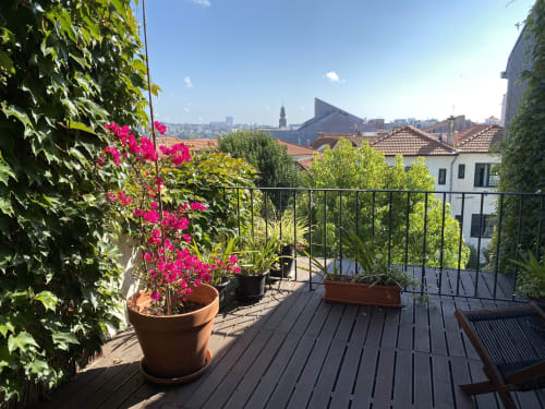 Terrasse ensoleillée de Casa45 à Porto avec fleurs roses, vue sur la ville et verdure luxuriante surplombant les toits historiques