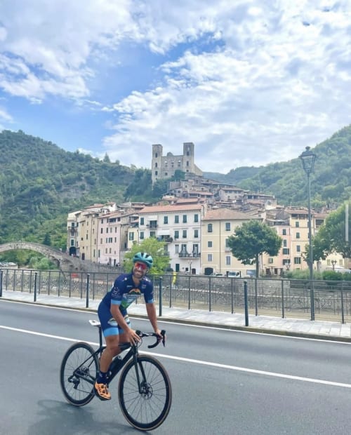 Ciclista su un ponte con vista sul castello di Dolceacqua e gli edifici colorati del villaggio nella valle italiana
