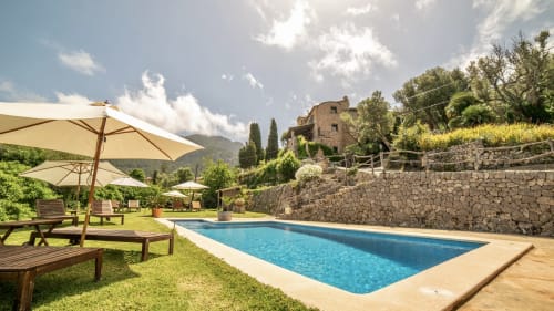 Zona de piscina del Petit Hotel Sa Plana en Estellencs con tumbonas, sombrillas y villa de piedra con vistas al campo de Mallorca