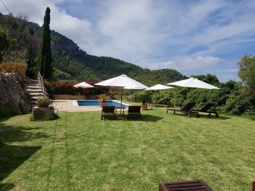 Exuberante jardín del Petit Hotel Sa Plana en Estellencs con piscina, sombrillas, tumbonas y vistas a las montañas