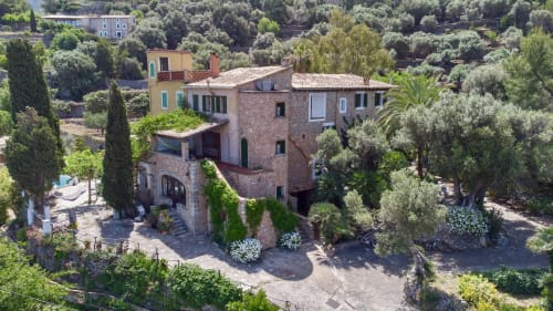 Petit Hotel Sa Plana en Estellencs, España: edificio de piedra rústica con tejado de barro rodeado de olivos y cipreses