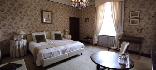 Élégante chambre du Château d'Hassonville avec papier peint fleuri, lit blanc, lustre et vue sur la cour