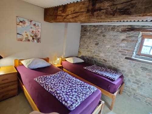 Chambre twin de l'appartement La Ferme De Werpin à Hotton, avec literie violette, poutres en bois et murs en pierre apparente