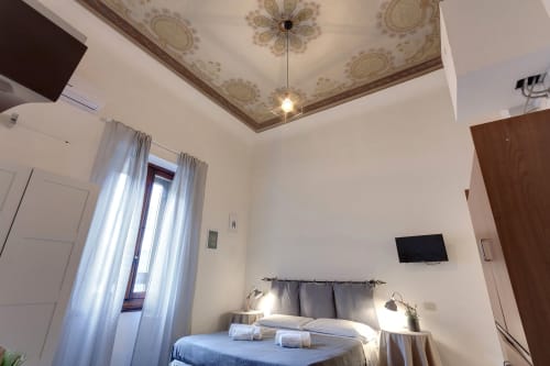 Sleep tight Florence studio apartment bedroom with ornate ceiling, TV, and modern amenities in Firenze