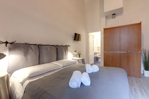 Modern studio apartment bedroom at Sleep tight Florence with queen bed, wooden wardrobe, and rolled towels in Firenze, Italy