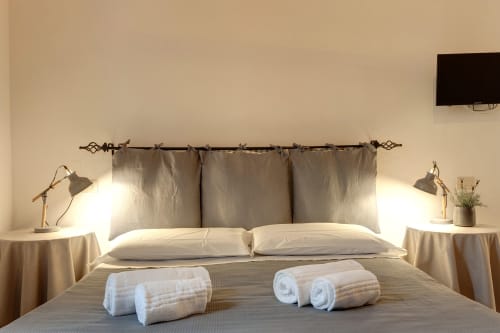 Modern bedroom at Sleep tight Florence with gray upholstered headboard, white pillows, rolled towels, bedside lamps, and TV