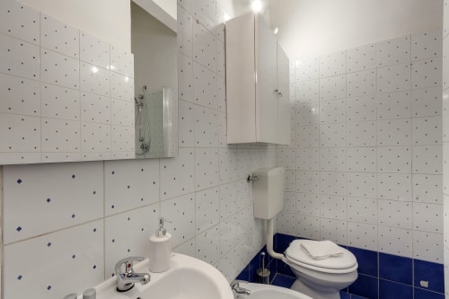 Modern bathroom in Sleep tight Florence studio apartment with white tiled walls, blue accents, sink, toilet, shower area, and