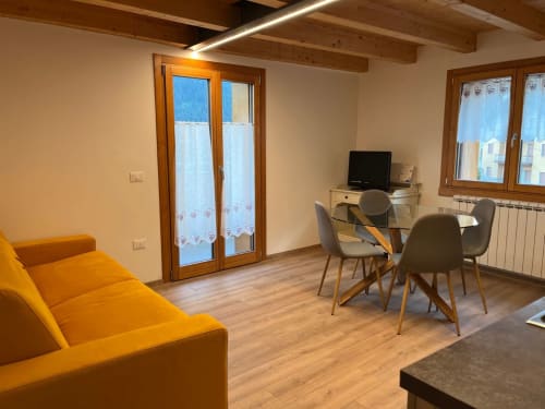 Moderno appartamento a La Corte di Vezza d'Oglio con divano arancione, zona pranzo, vista montagna e travi in legno