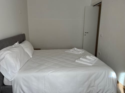 Camera da letto luminosa con biancheria bianca e testata grigia presso l'appartamento Residence La Corte a Vezza d'Oglio, Italia