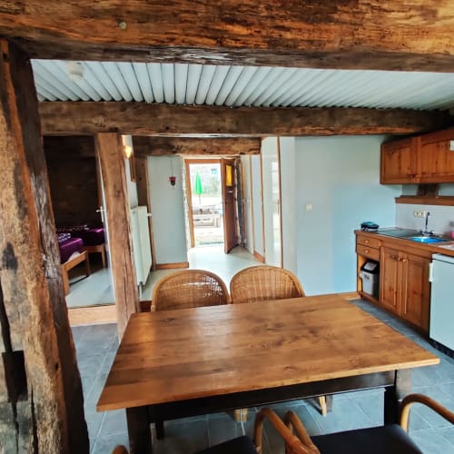 Salle à manger du rez-de-chaussée avec table en bois, chaises en osier, cuisine et accès au jardin à La Ferme De Werpin
