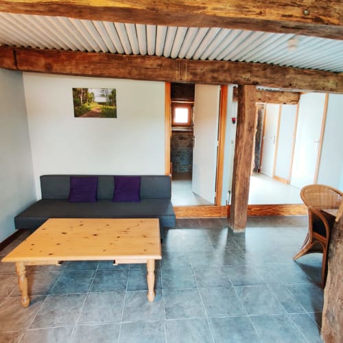 Salon au rez-de-chaussée avec canapé gris, table en bois et fauteuil en rotin à La Ferme De Werpin, Hotton