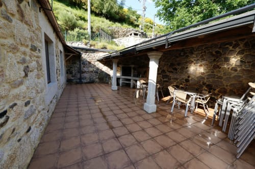 Terraza cubierta con suelo de baldosas de barro, muros de piedra y zonas de descanso en la finca rural Balbino de León, España